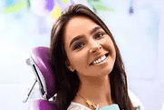 Smiling woman with dark hair in dental office setting wearing purple dental bib.