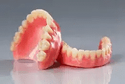 Two complete dentures displayed on gray surface showing pink gum base and artificial teeth.