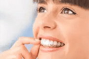 Young person flossing teeth with white dental floss, smiling brightly against light blue background.