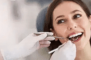 Woman smiling while brushing teeth with toothbrush in bright, clean dental setting.