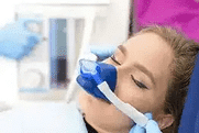 Patient receiving dental treatment in clinical setting with dentist wearing blue gloves and mask.