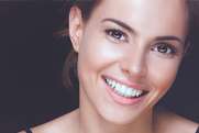 Smiling woman with bright teeth in professional headshot against dark background for dental practice