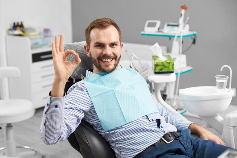 Happy patient giving an OK sign in a modern dental office treatment room.