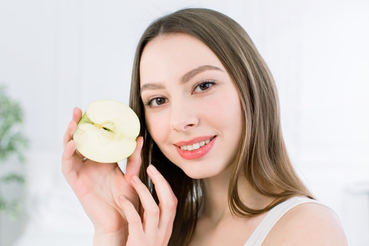Woman holding yellow soap bar smiling at camera in bright bathroom setting.