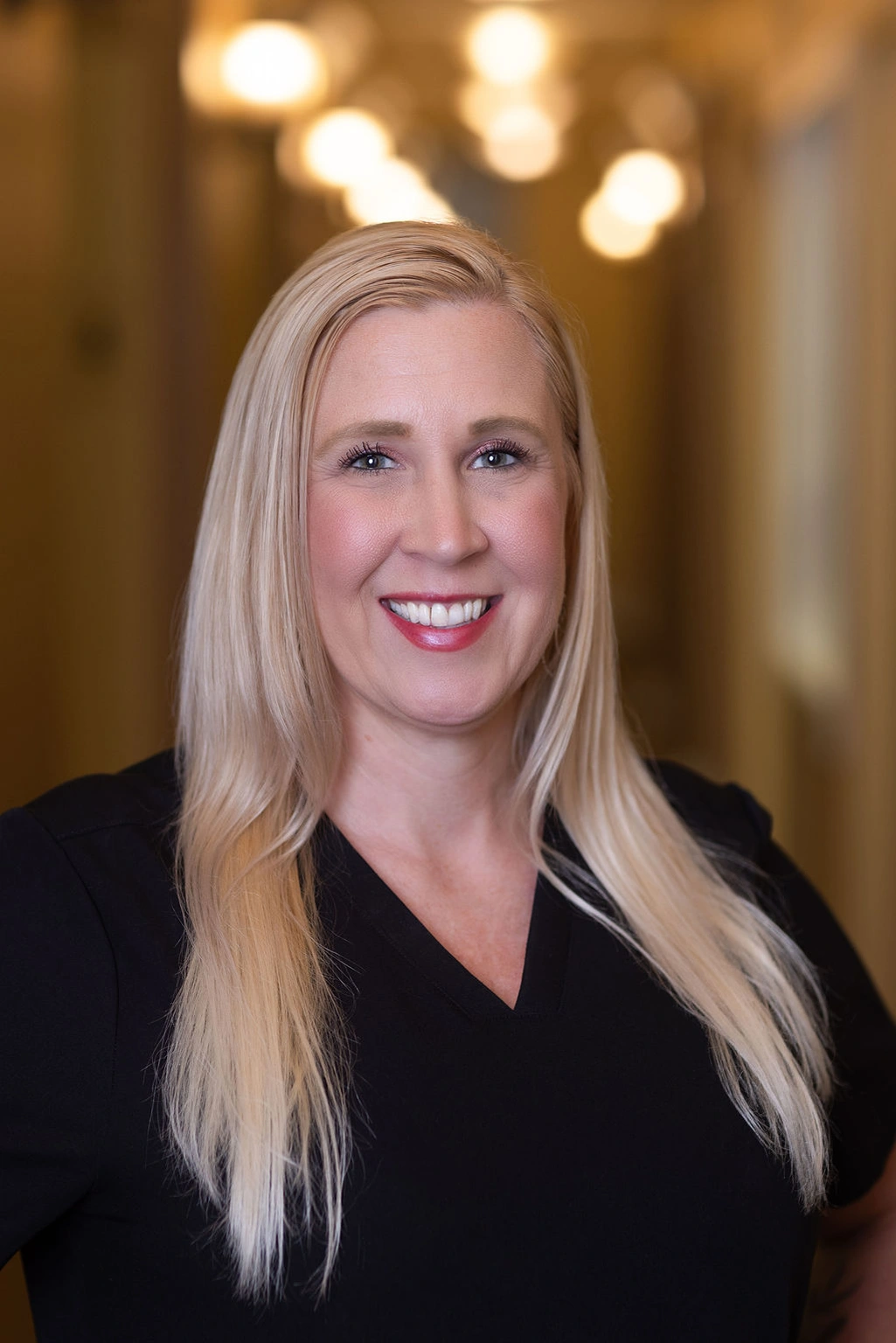 Professional headshot of woman with long blonde hair smiling in dental office setting.