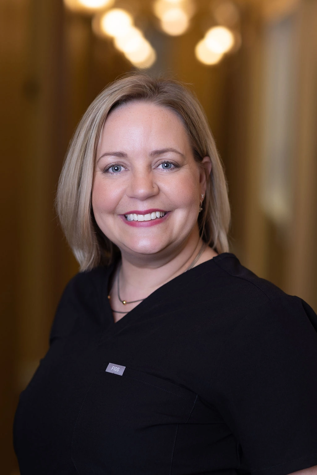 Professional portrait of a woman smiling in dental office setting with warm lighting.