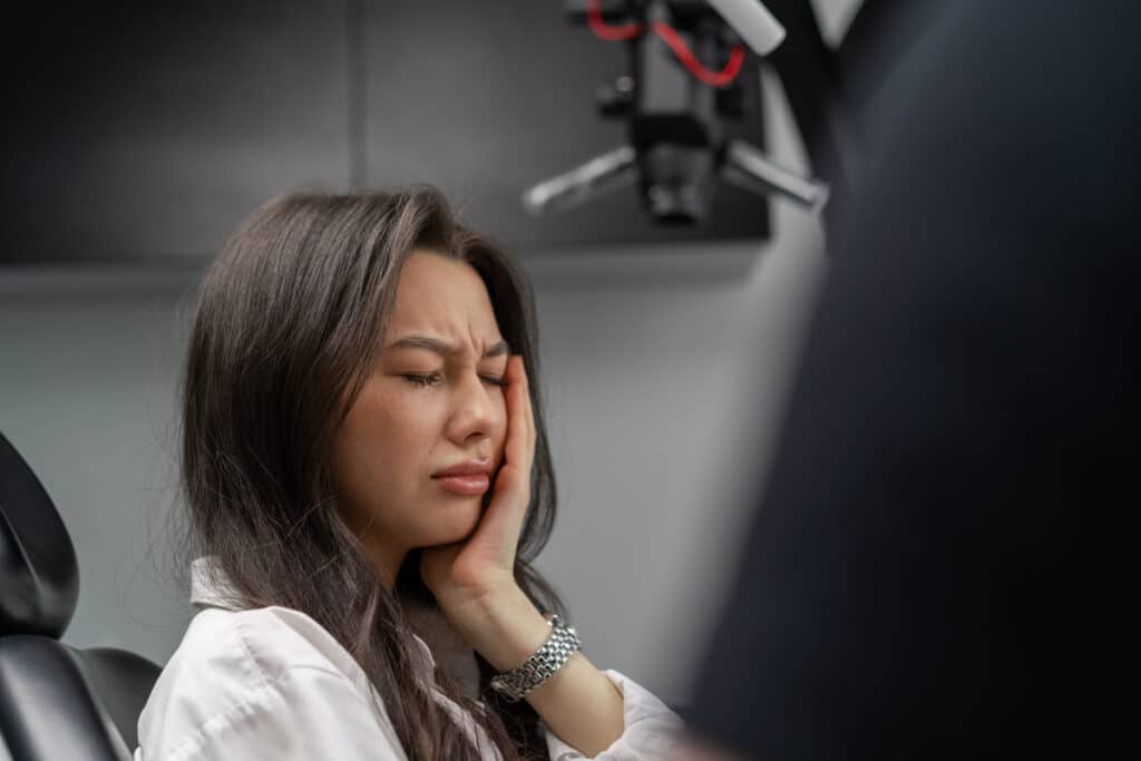 Woman experiencing jaw pain or discomfort during dental consultation related to liver disease complications.