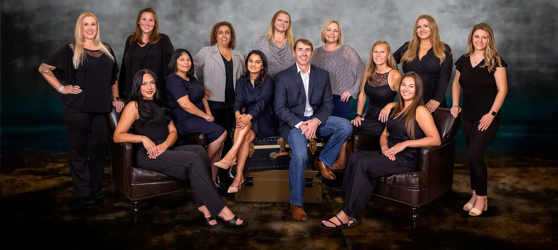 Professional dental team portrait in formal black attire against dark background studio setting.