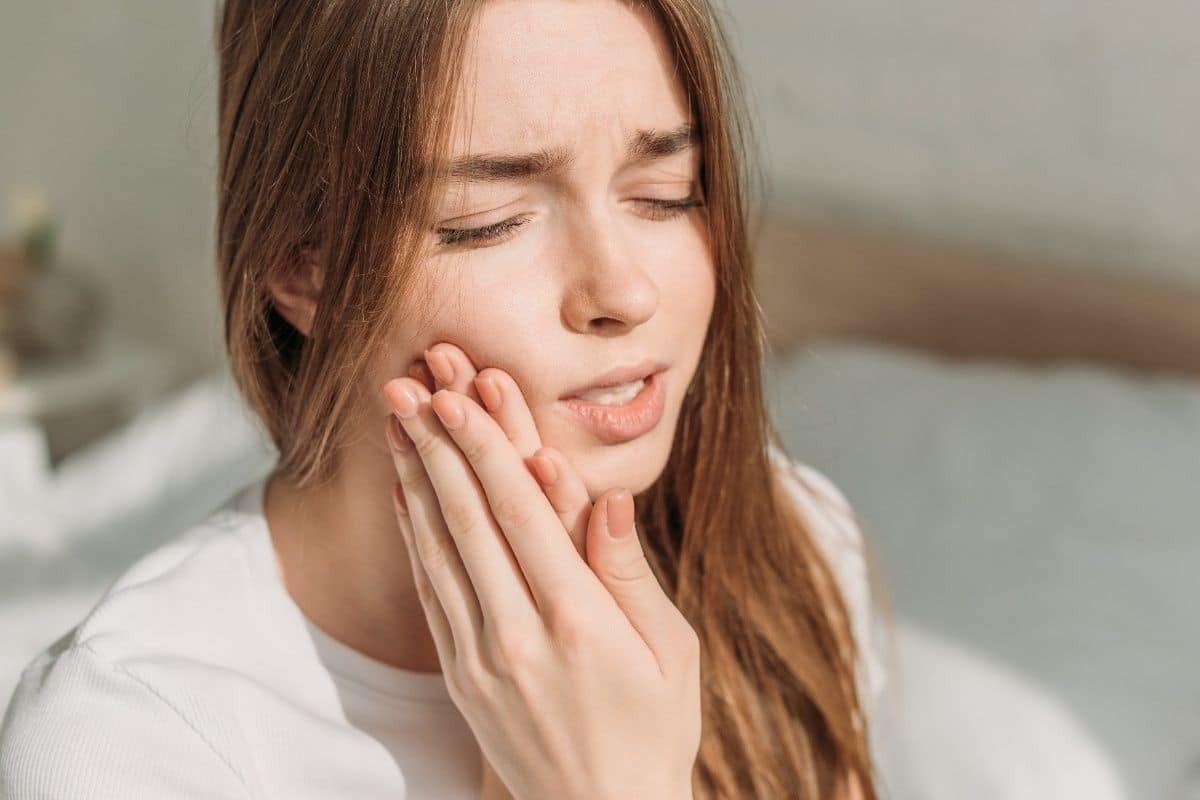 Woman experiencing severe tooth pain, holding her cheek in discomfort.
