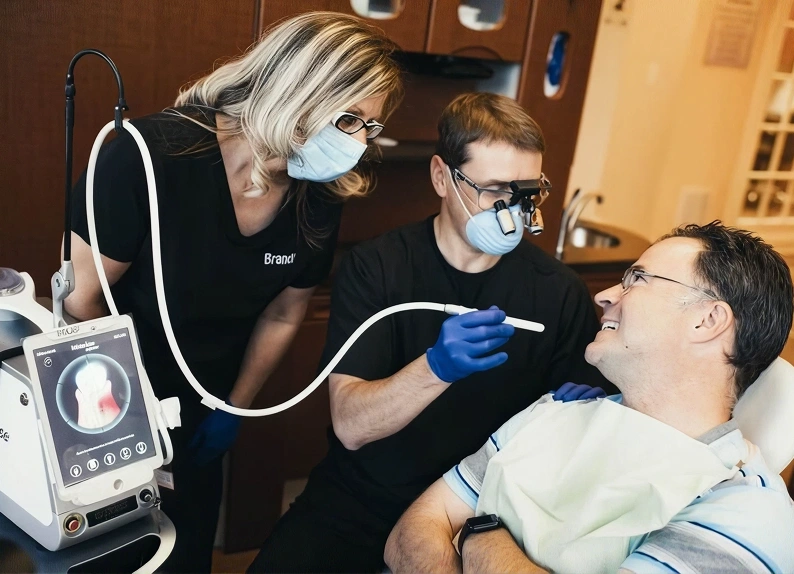 Dentist using advanced dental technology to examine a patient while a dental assistant observes.